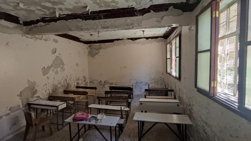Damaged classroom with broken ceiling and empty desks, showing disruption to education in a conflict-affected area. (Syria, 2022)