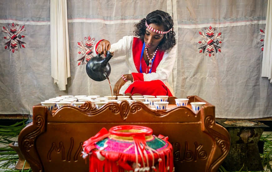 Une femme vêtue d'un costume traditionnel éthiopien verse du café dans des tasses.