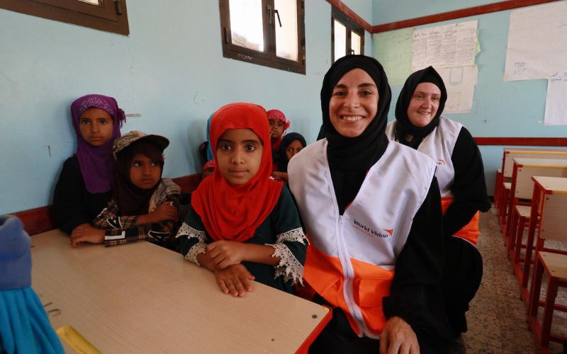 Des enfants et des employés de World Vision sourient dans une salle de classe.