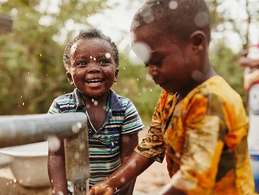 Child smiling next to a water pump.