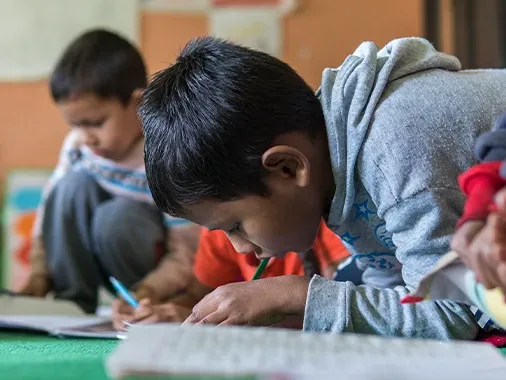 Child writing on desk at school.