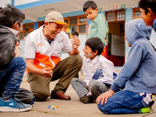 A World Vision staff member and young boys are playing jackstones on the floor.