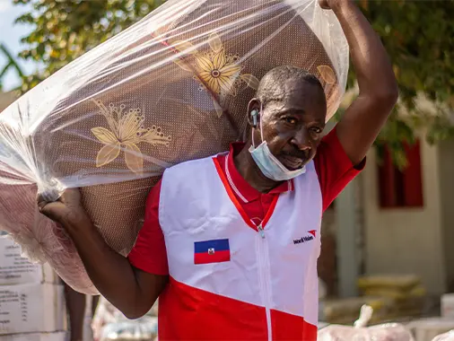 A World Vision staff is carrying a sleeping mat.