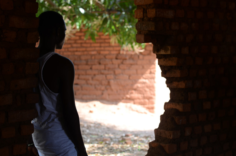 Un jeune homme, ancien enfant-soldat au Soudan du Sud, est adossé à un mur de briques en ruine.