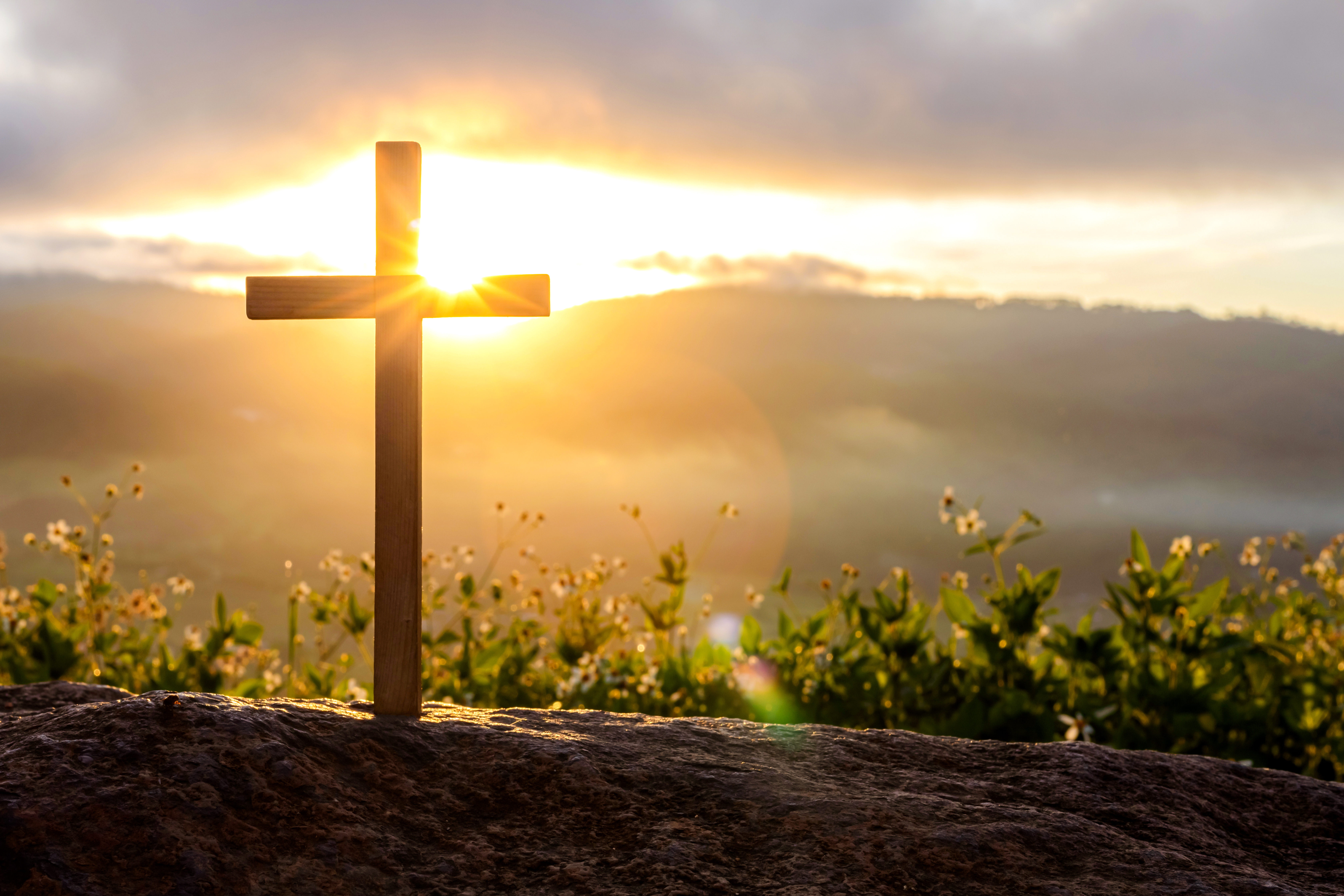 Une croix de bois sur une montagne au lever du soleil. La lumière perce au-dessus des collines lointaines, symbolisant le dimanche de la Résurrection.