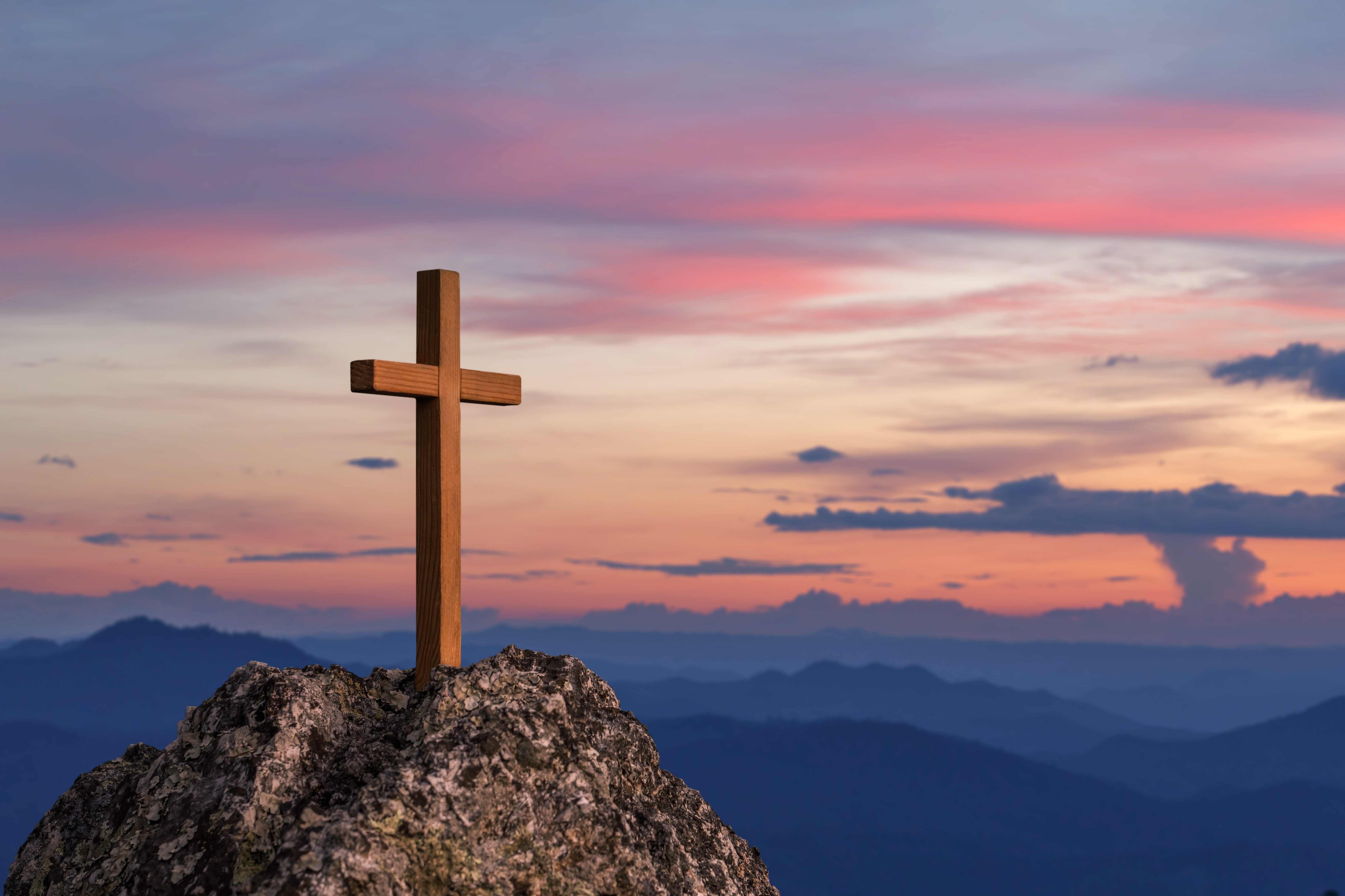Une croix en bois au sommet d’une colline rocheuse, sous un lever de soleil éclatant et haut en couleur.