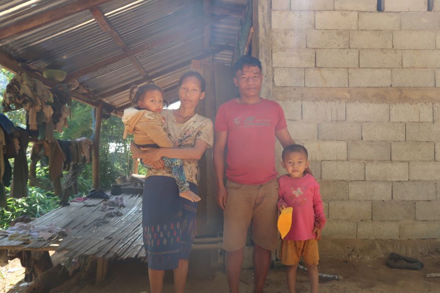 Au Laos, une mère et un père se tiennent devant une maison en parpaings avec leurs deux jeunes enfants.