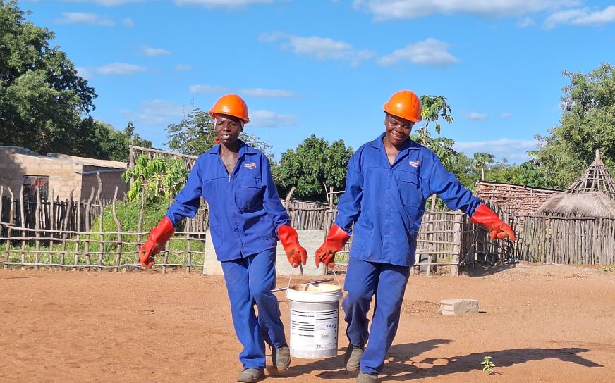 Dans le sud du Mozambique, deux femmes vêtues d’une tenue de travail bleue et portant des casques de chantier orange transportent un seau de ciment.