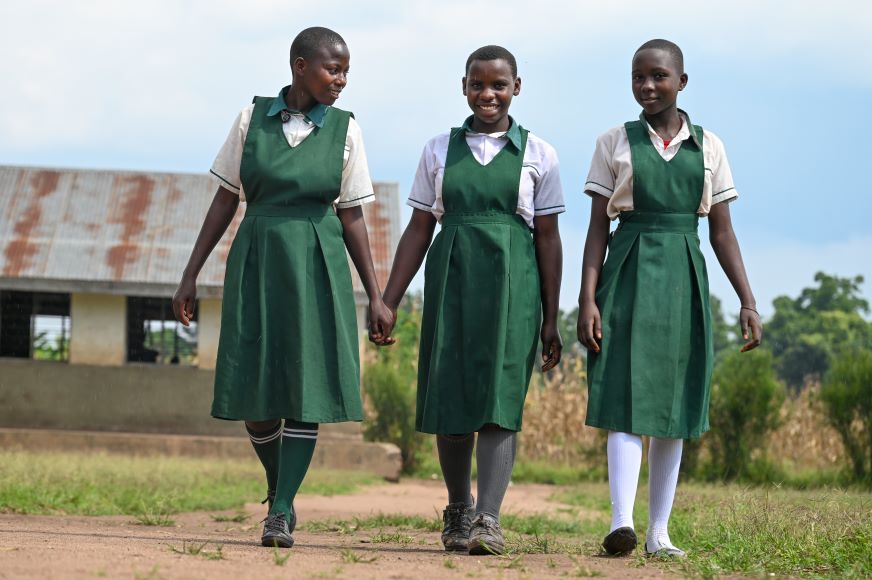 En Ouganda, trois adolescentes vêtues d’uniformes scolaires verts marchent côte à côte.