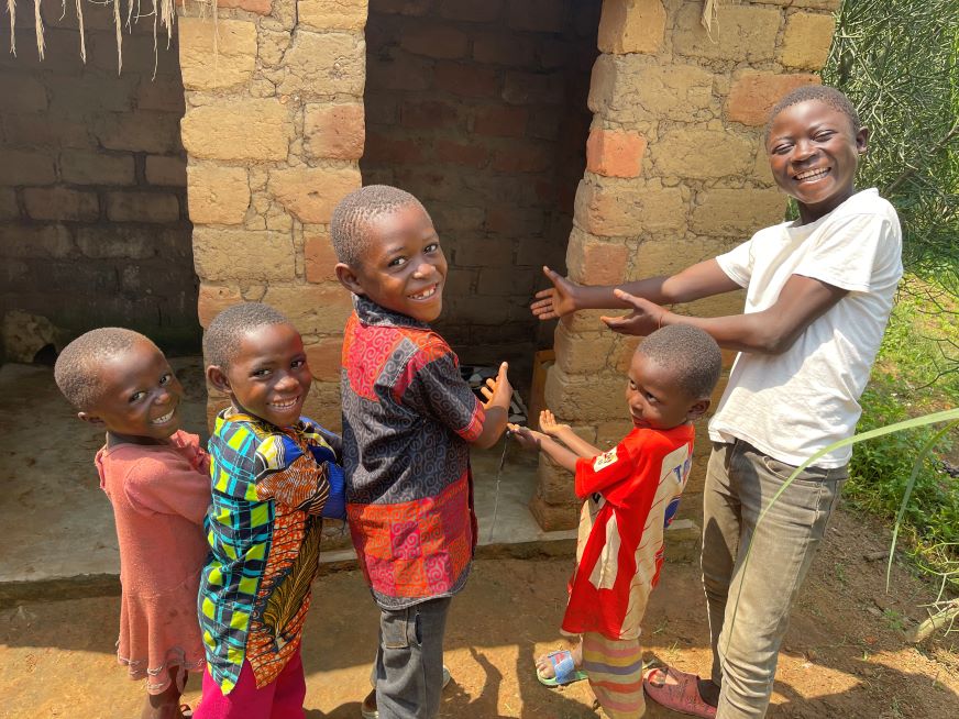 En République démocratique du Congo, cinq enfants sourient en montrant du doigt une nouvelle latrine en briques.