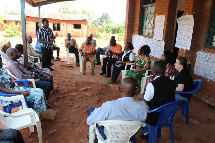 À Makamba, au Burundi, un groupe d’adultes est assis sur des chaises en plastique à l’extérieur, tandis qu’un homme, debout, s’adresse au groupe.