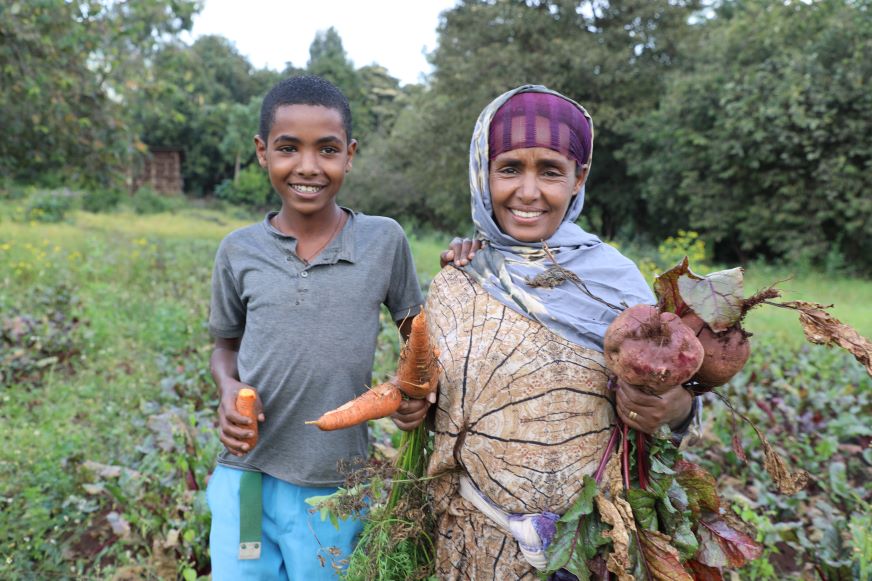 À Oda Bultum, en Éthiopie, une mère et son fils se tiennent dans leur potager, tenant dans leurs mains des betteraves et des carottes fraîchement cueillies.