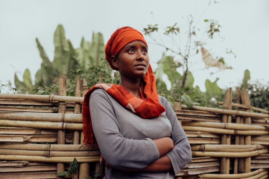 Une adolescente portant un foulard rouge regarde droit devant elle, l’air déterminé, les bras croisés.