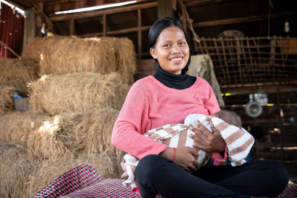 Dans le district de Pouk, au Cambodge, une mère est assise sur une natte dans une grange, en train d'allaiter son bébé.