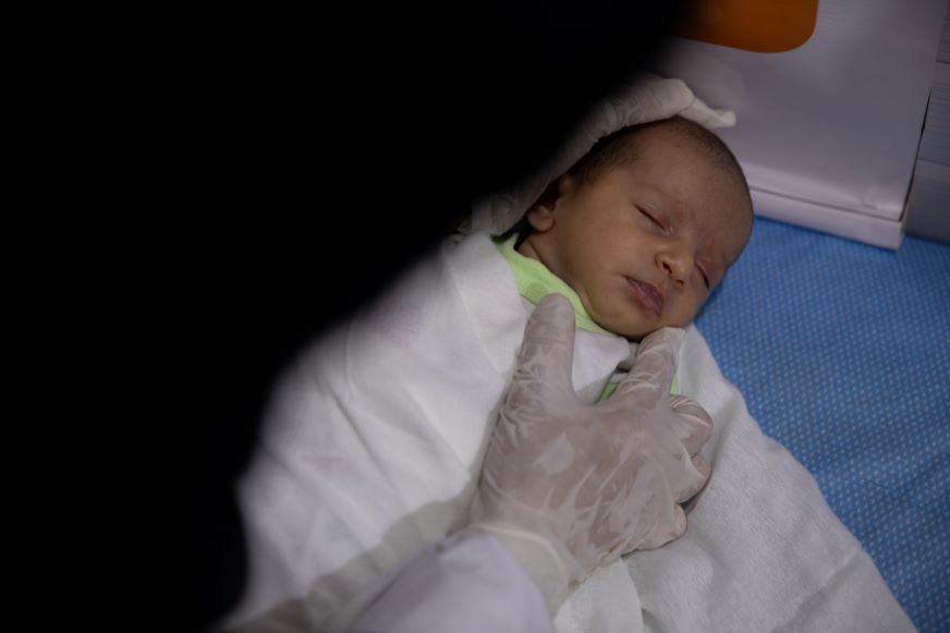 Un nouveau-né endormi est bercé par un professionnel de la santé portant des gants.