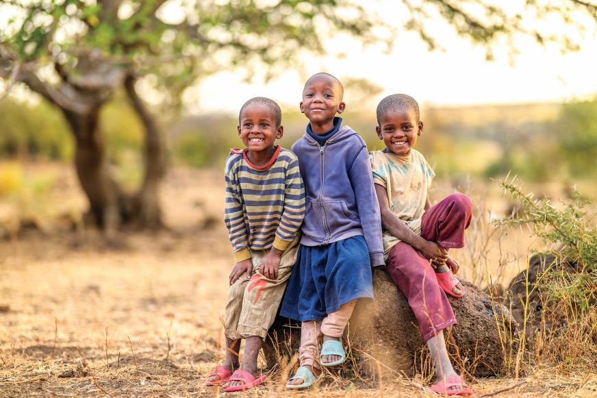Trois enfants sont assis ensemble, tout sourire, dans une région rurale de la Tanzanie.