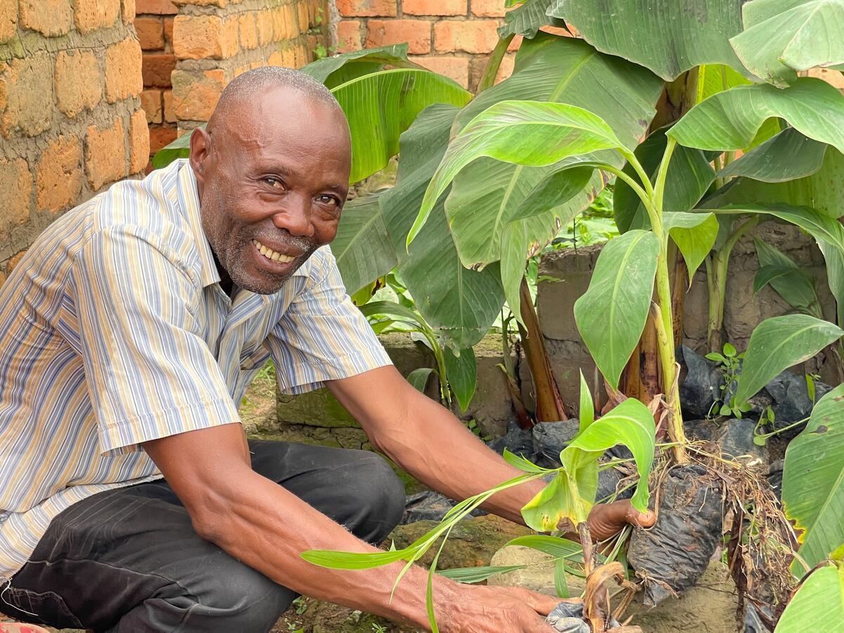 Un homme tenant un jeune plant de bananier – WVC : de l’agriculture à l’éducation