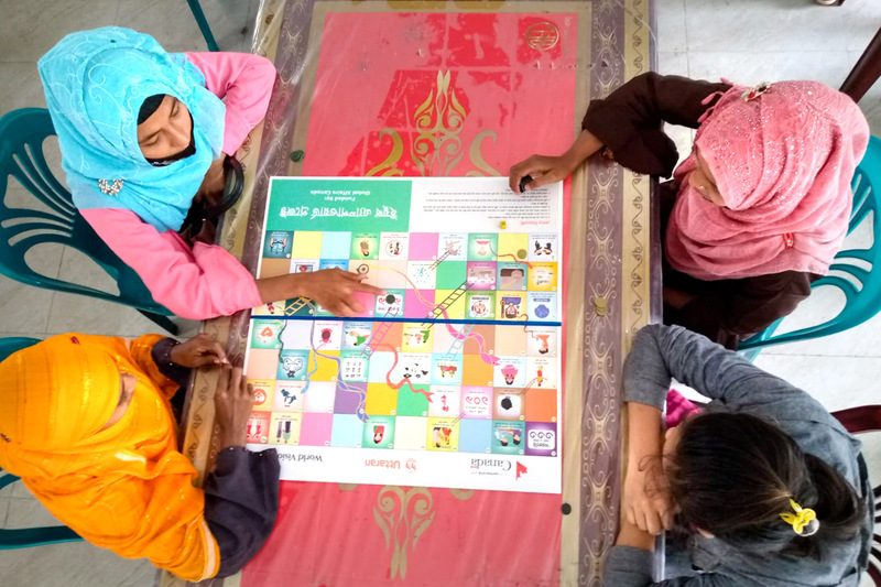 Vue d’en haut, on voit quatre filles assises à une table, en train de jouer à un jeu de société coloré.