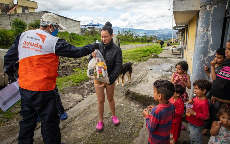 Un membre de l'équipe de World Vision remet un sac de provisions à une femme en Équateur. Sept enfants se tiennent à proximité.