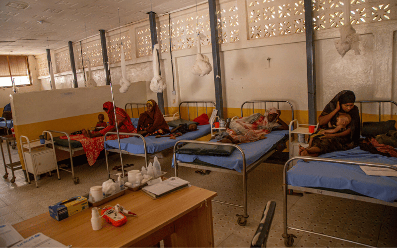 Quatre femmes somaliennes, accompagnées de leurs enfants, sont assises ou allongées sur des lits dans un centre de santé.