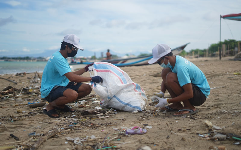 Deux hommes de l'organisme « The Ocean Clean-up Group », à Bali, en Indonésie, s'accroupissent pour ramasser des déchets sur la plage.