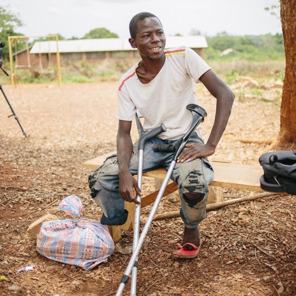 Un homme centrafricain, qui n'a qu'une jambe, est assis sur un banc, ses béquilles à la main.