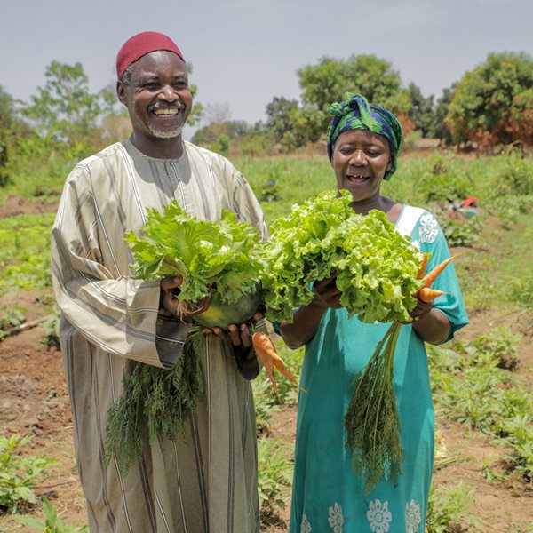 Un homme et une femme en République centrafricaine sourient, des légumes à la main.