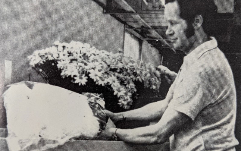 Image en noir et blanc d’un homme en train d’emballer des fleurs en vue de leur livraison.
