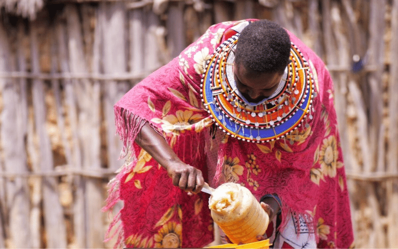 Une femme vêtue d'une robe aux couleurs vives verse du miel dans un récipient.