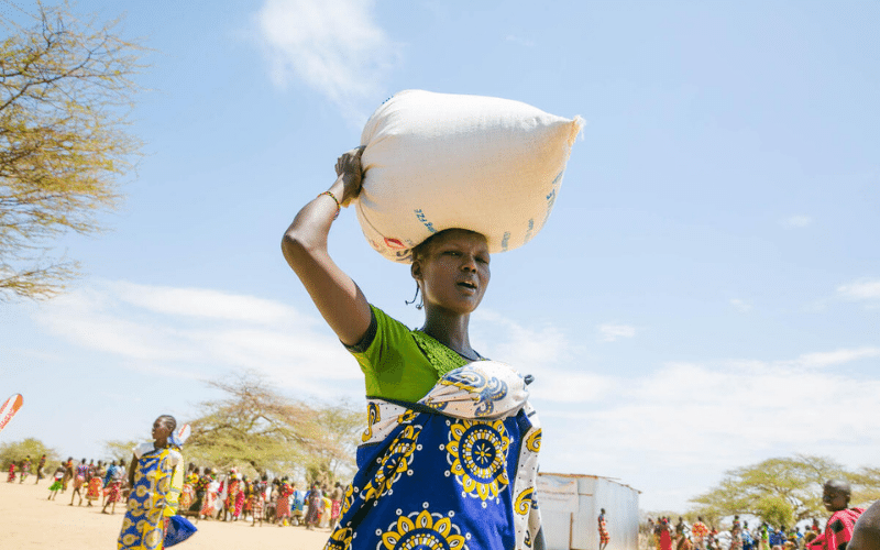 Une femme marche en portant un sac de céréales sur la tête.