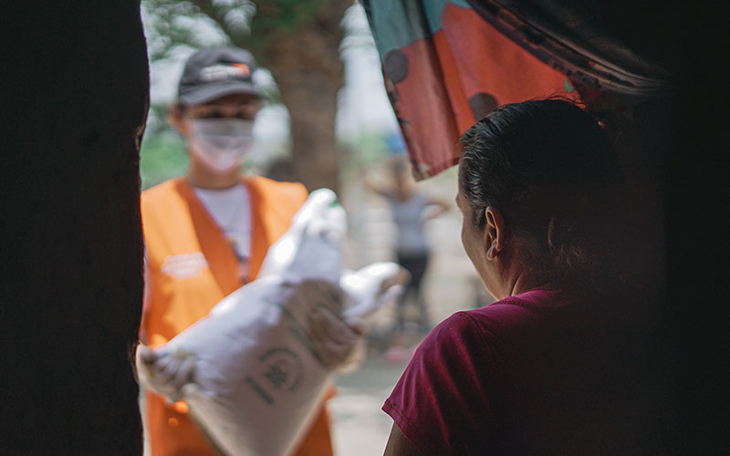 Au Honduras, une mère ouvre la porte à un intervenant de World Vision qui porte un sac de graines.