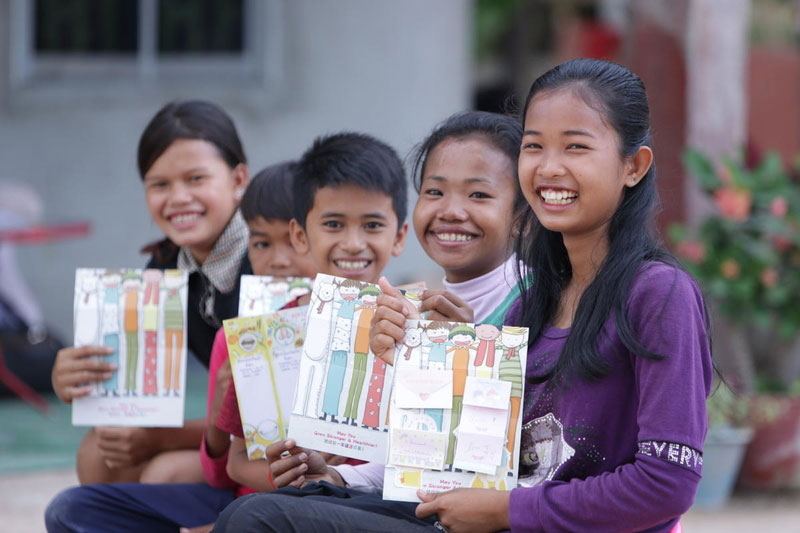 Cinq enfants du Cambodge montrent fièrement leurs cartes de Noël colorées.
