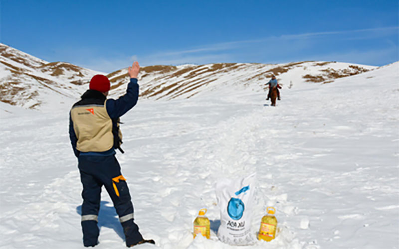 Un employé de World Vision, vêtu d’un pantalon de neige et d’un chapeau de laine, fait signe à un homme qui descend des montagnes à dos d’animal.