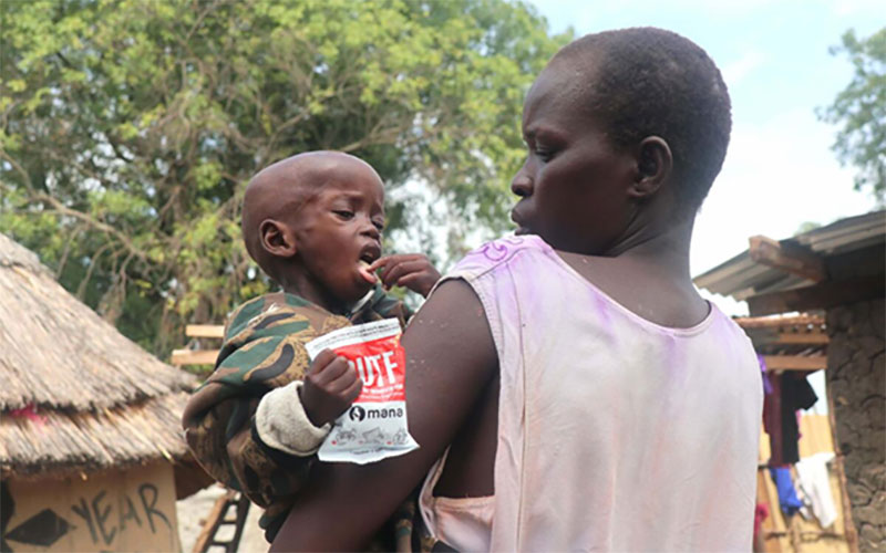Au Soudan du Sud, une mère tient son jeune enfant dans ses bras. Celui-ci tient un paquet d’aliments prêts à consommer et riches en nutriments.