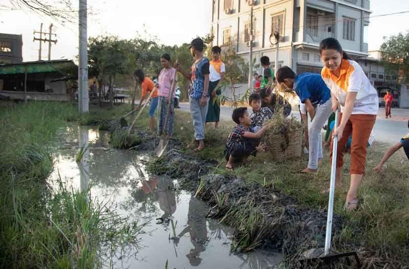 Un groupe d'enfants et d'adolescents nettoie un ruisseau à l'aide de râteaux et de houes.
