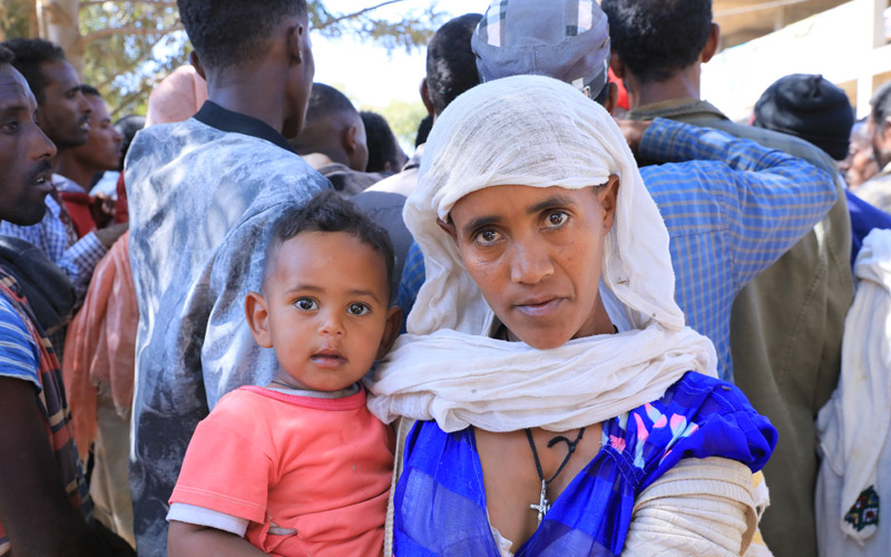 Une Éthiopienne tient un bébé dans ses bras. Derrière elle, se trouve une foule d’hommes et de garçons.