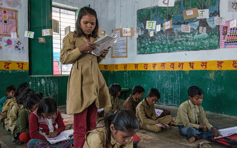 Une jeune Indienne se tient debout dans sa classe et lit à haute voix le livre qu’elle tient à la main.