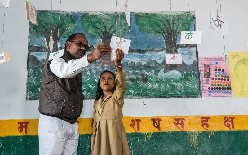 Une jeune Indienne se tient à côté de son enseignant dans la salle de classe pendant qu’ils travaillent sur une leçon.