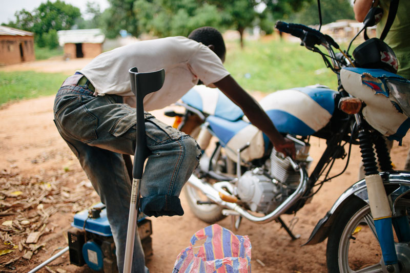 Un jeune homme qui a subi une lésion permanente à la jambe droite est en train de réparer une moto.