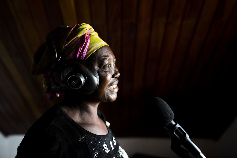 Une femme portant un foulard jaune et rose utilisait des écouteurs et enregistrait de la musique dans un studio.