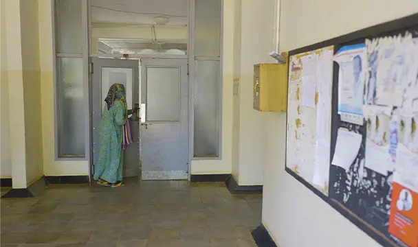 A women holding a bag, begins to open a door at the far end of the room.