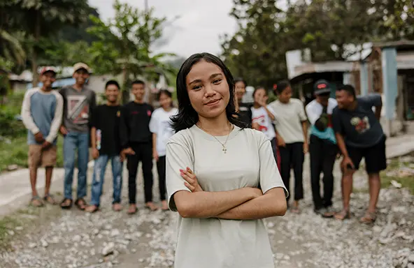 A girl in a white shirt, crosses her arms and smiles. (Indonesia, 2023)