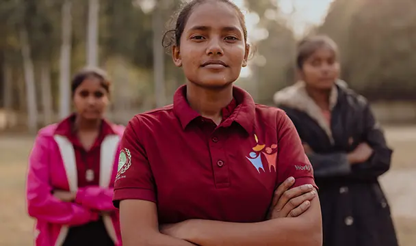 Neha stands confidently with two teenage girls, their arms crossed.