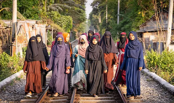 A group of Bangladeshi girls, wearing hijabs and niqabs, walk together on a path.
