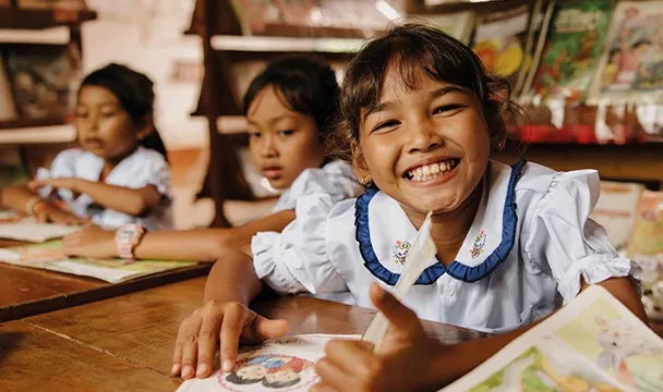 Three girls wearing school uniform are in a library reading books.