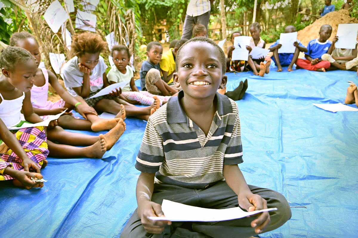 Junior sourit, ses devoirs à la main, aux côtés de ses camarades de classe, lors d’une séance du club de lecture. 