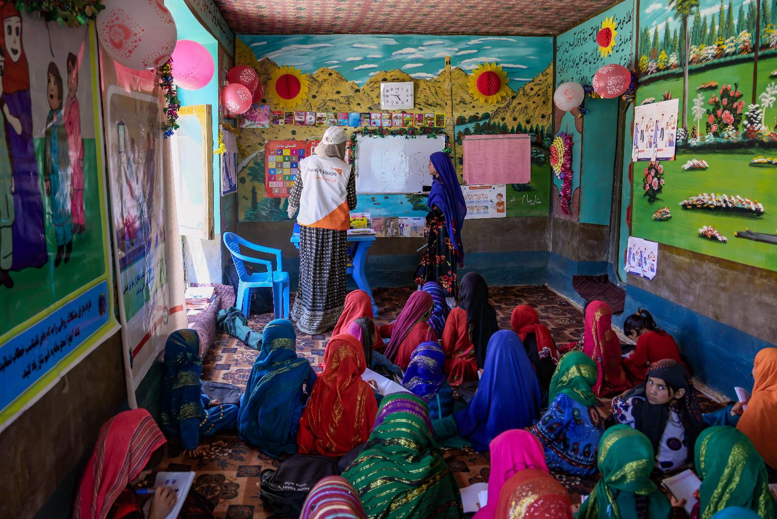 Children sit on a carpeted floor in a child-friendly space.
