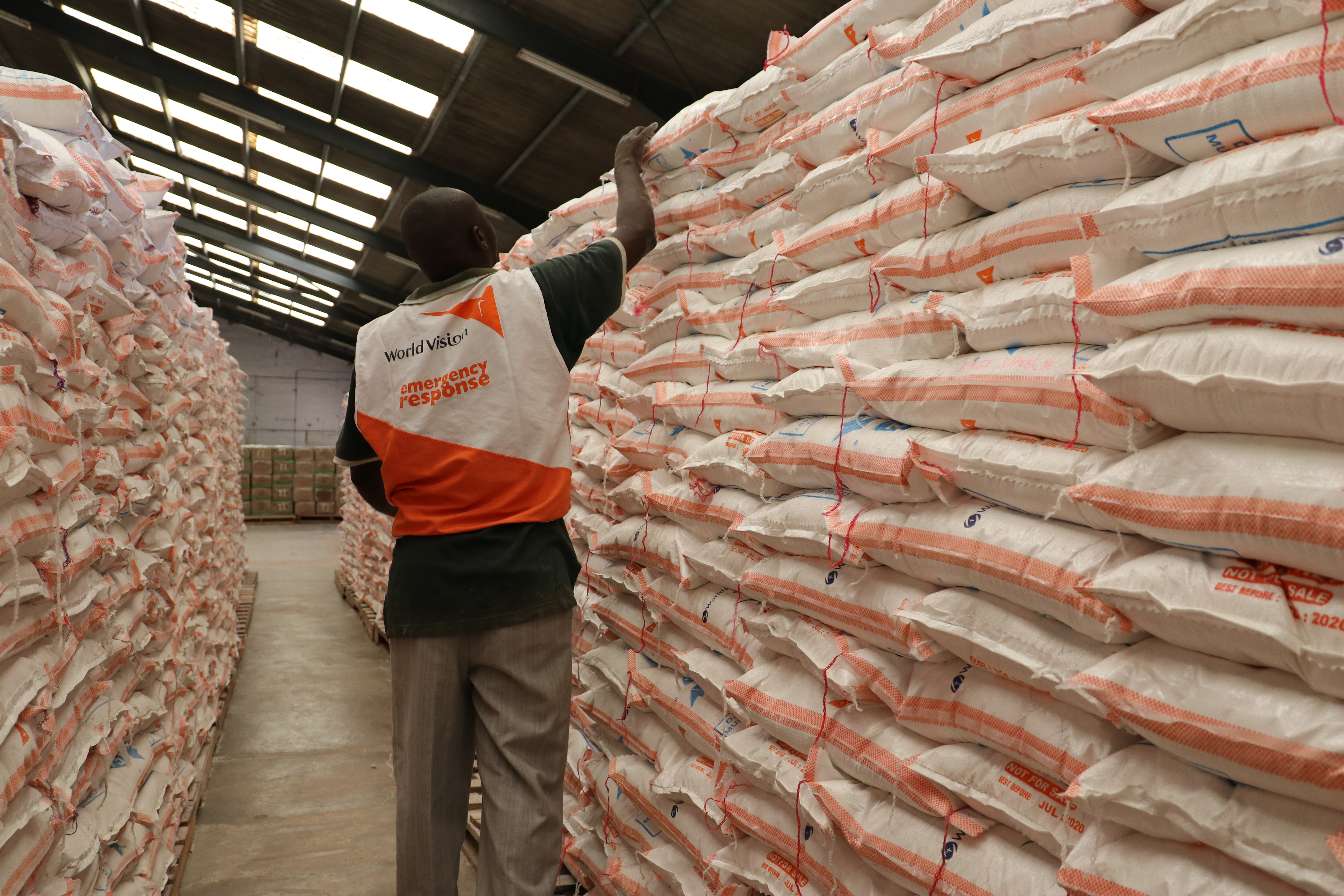 A man in World Vision vest inspects life-saving food supplies in a warehouse in Zambia's southern province as part of emergency response.