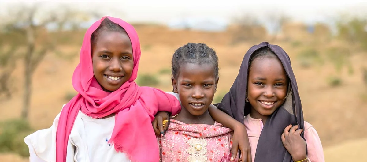 Three girls stand together with hope outside in Africa.