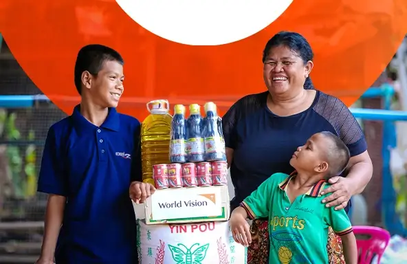 A mother and her two sons smile while standing around a pile of packaged food.